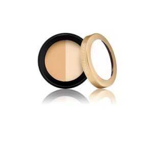 Two-tone concealer duo in a round black compact with a gold lid, open to reveal beige shades and mirror reflection.