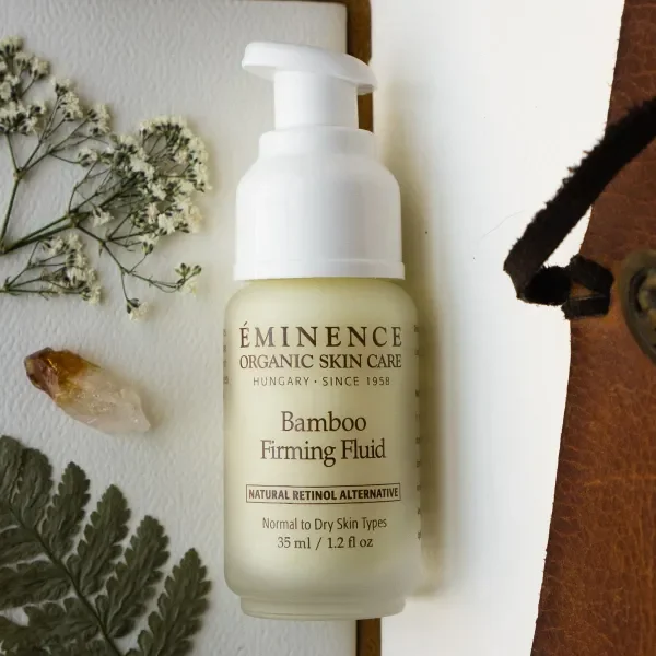 Bamboo-firming-fluid-6_2 – Damara Luxury Spa Vancouver Bottle of Eminence Bamboo Firming Fluid with pump, placed on a white surface with dried flowers and ferns nearby.