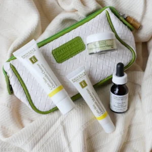 White quilted bag with lime-green trim holding Eminence Organic Skin Care tubes, a small jar, and a dropper bottle on a soft beige blanket.