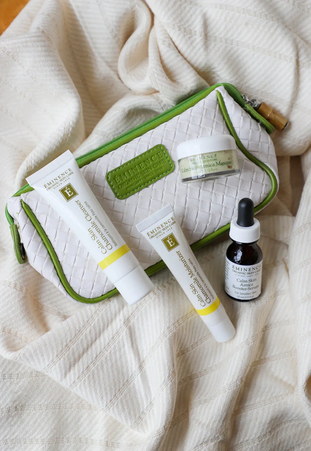 CalmSkinStarterKit2 – Damara Luxury Spa Vancouver White quilted bag with lime-green trim holding Eminence Organic Skin Care tubes, a small jar, and a dropper bottle on a soft beige blanket.