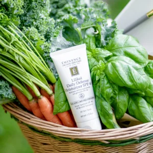 Tube of Eminence Daily Defense Moisturizer SPF 40 nestled in a basket with kale, spinach, and carrots.