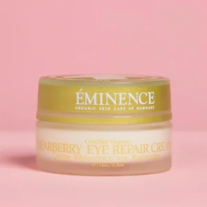 Close-up of a jar labeled Eminence Organic Skin Care with a gold lid on a pink background, Eye Repair Cream visible on the label.