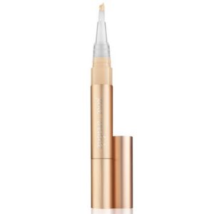 Gold-toned concealer pen with beige liquid and slender brush applicator, standing upright.