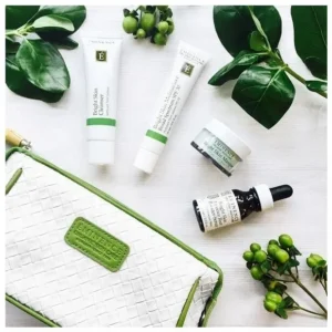 Assorted skincare products arranged around a white woven bag on a light surface, with green leaves and berries in the background.
