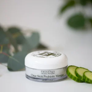 Jar of Eminence Clear Skin Probiotic Masque on a white surface with cucumber slices nearby and soft green leaves in the background