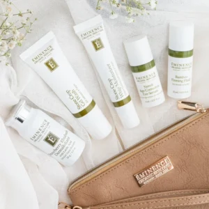 Assortment of Eminence Organic Skin Care tubes and bottles laid out on light fabric beside a tan zippered pouch