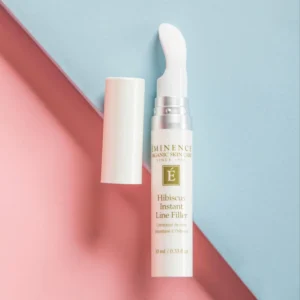White bottle with a wand applicator (cap removed) for Hibiscus Instant Line Filler, set against a pink and blue pastel background, close-up product shot
