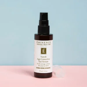 Eminence Neroli Age Corrective Eye Serum bottle with pump on a pastel pink and blue background.