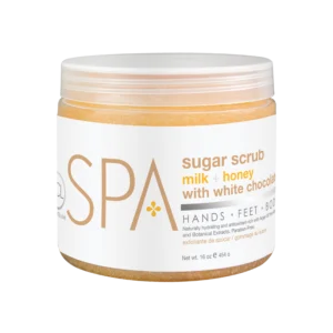 Cosmetic sugar scrub jar with label reading 'milk + honey with white chocolate' and 'Spa' branding, 16 oz (454 g) inside a clear amber jar